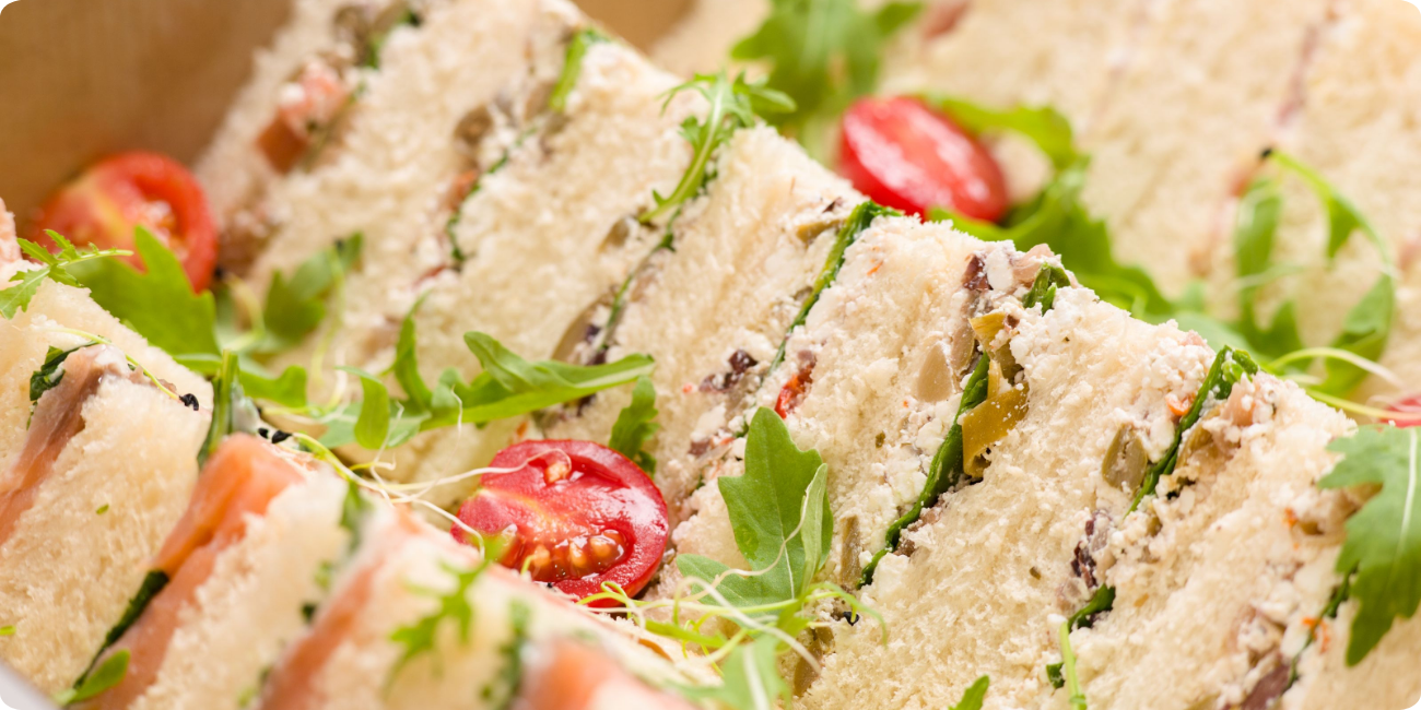 A box containing assorted sandwiches filled with fresh tomatoes and greens, arranged neatly for serving
