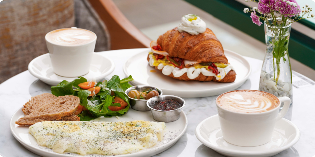 A breakfast table displaying a croissant, a colorful salad, and a steaming cup of coffee