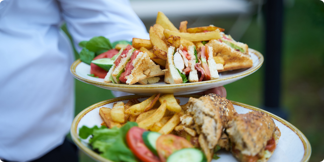 A waiter presents two plates of sandwiches accompanied by chips, showcasing a delicious meal option