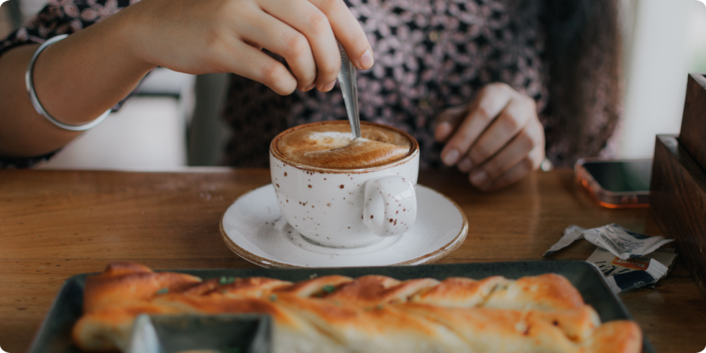 A woman prepares to stir her coffee with a spoon, showcasing a warm café atmosphere