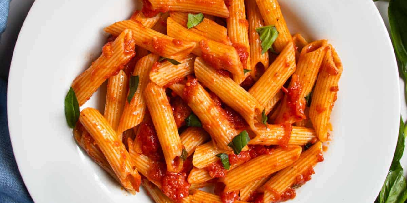 A bowl of penne pasta topped with rich tomato sauce, garnished with fresh basil leaves