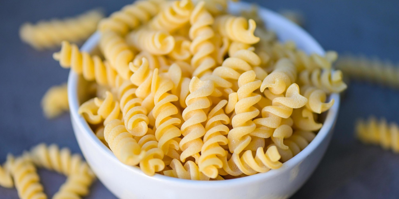 A bowl of uncooked fusilli pasta placed on a wooden table, showcasing its spiral shape and texture