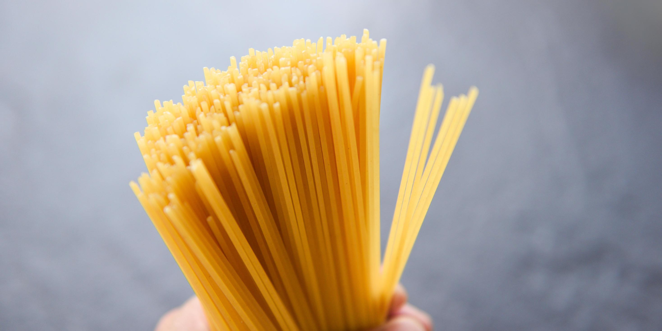 A close-up of a person holding uncooked spaghetti, emphasizing the texture and shape of the noodles