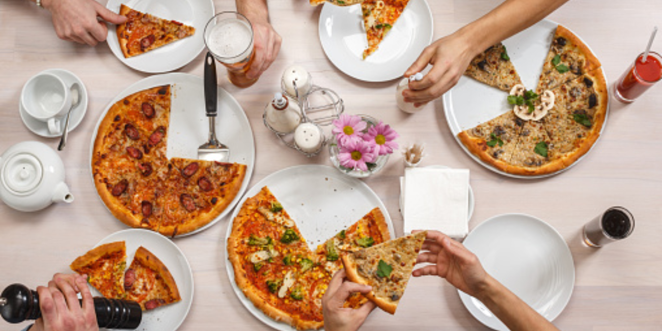 A diverse group of individuals seated at a table, sharing slices of pizza and enjoying each other's company.