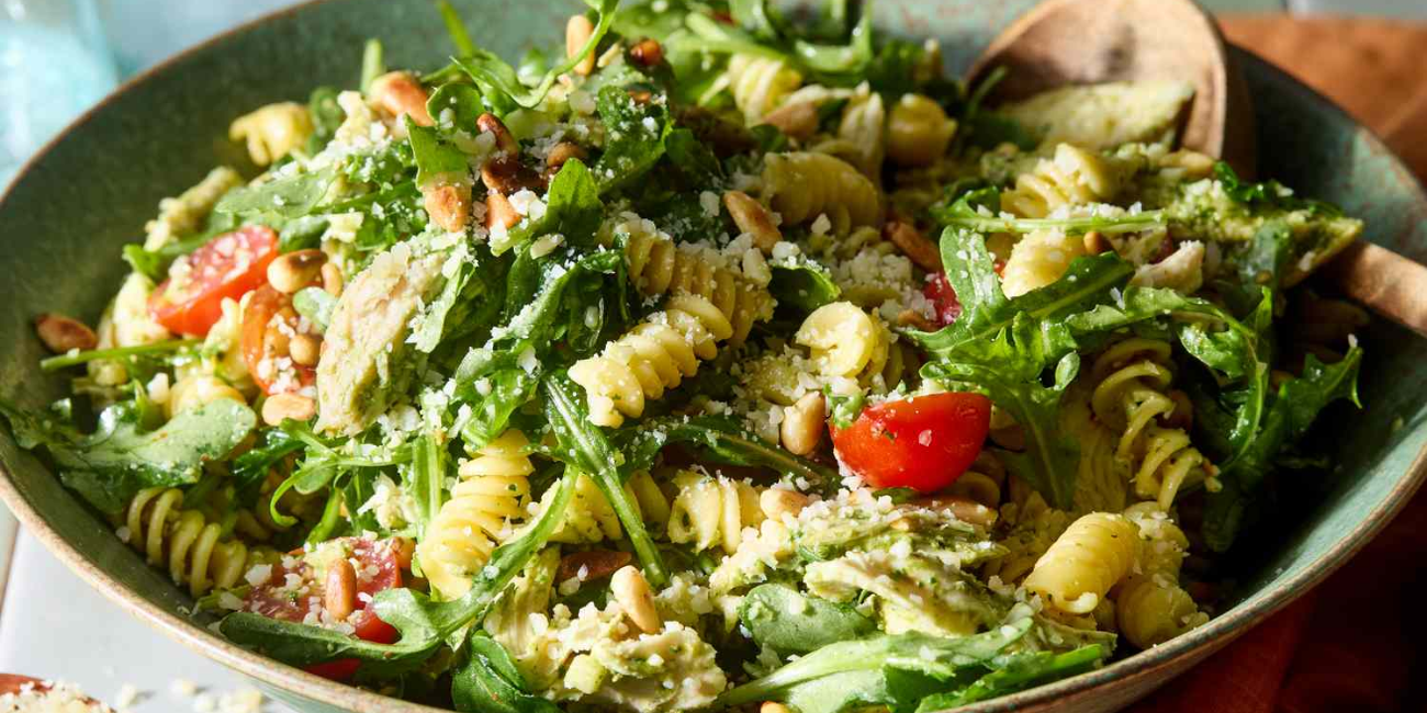 A vibrant bowl of pasta salad with pesto, cherry tomatoes, pine nuts, and sprinkled parmesan cheese