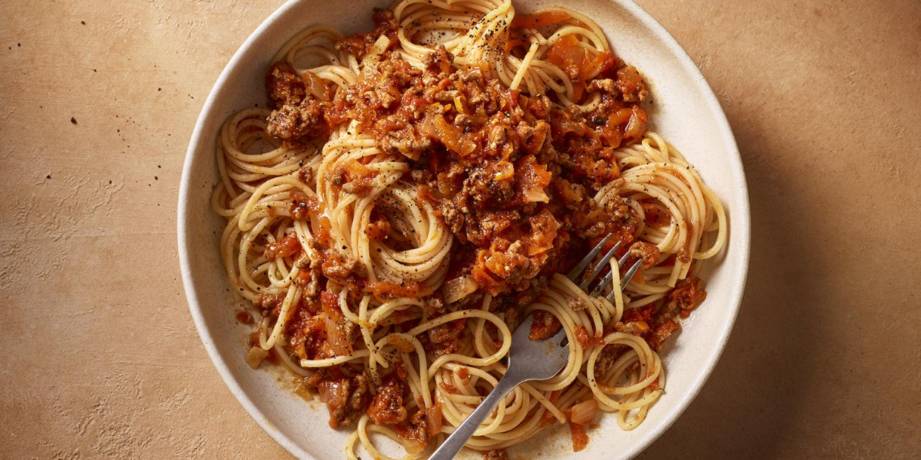 A white bowl filled with spaghetti topped with rich chicken sauce, garnished with herbs