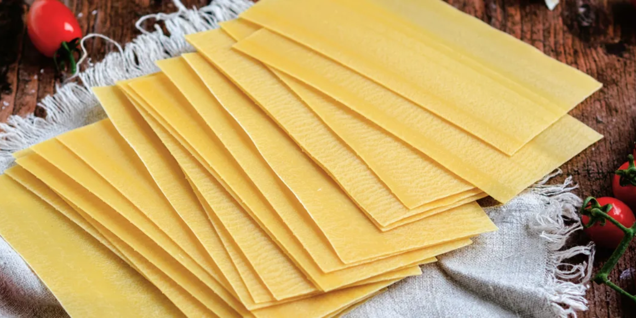 A white napkin holds uncooked lasagne sheet and sliced red peppers, ingredients for an uncooked lasagne dish