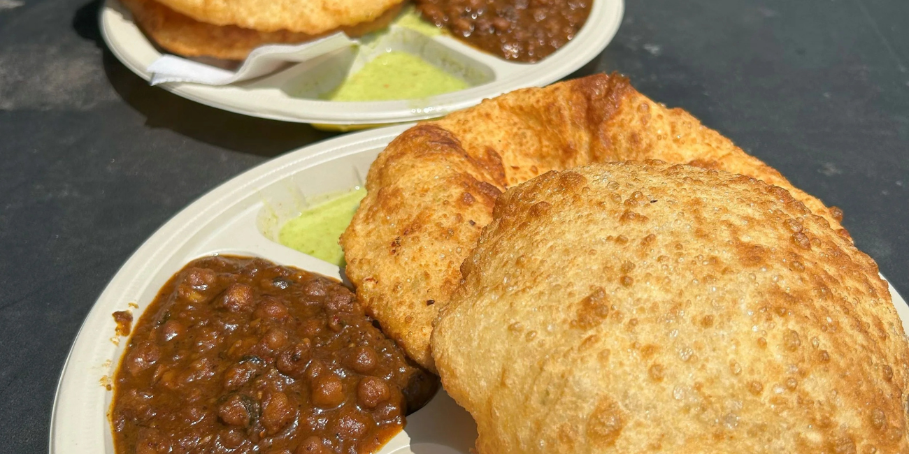 Two plates of Indian chole bhature: golden, puffed fried breads served with dark chickpea curry and green chutney, creating a hearty, appetizing meal.
