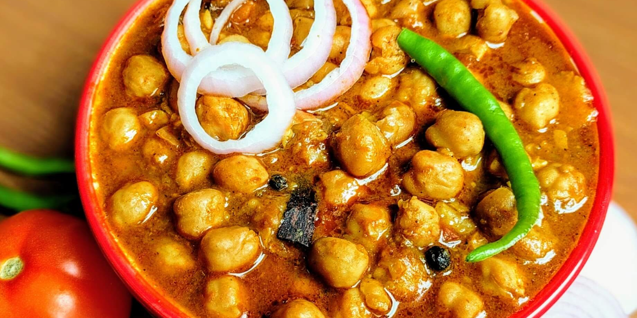A vibrant bowl containing assorted beans, fresh vegetables, diced onions, and ripe tomatoes, emphasizing nutritious ingredients.